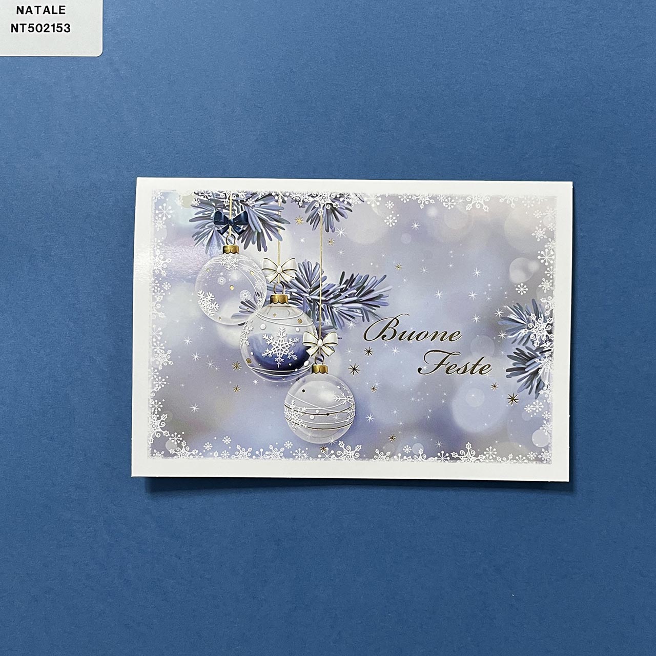 Biglietto di Natale personalizzabile orizzontale. Copertina lucida sui toni del blu con illustrazione moderna di tre palline appese e piccoli particolari a rilevo dorati.